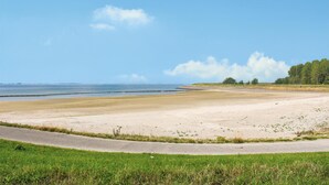 Eine Küstenlandschaft mit Sandstrand, grasbewachsenem Vordergrund und blauem Himmel.