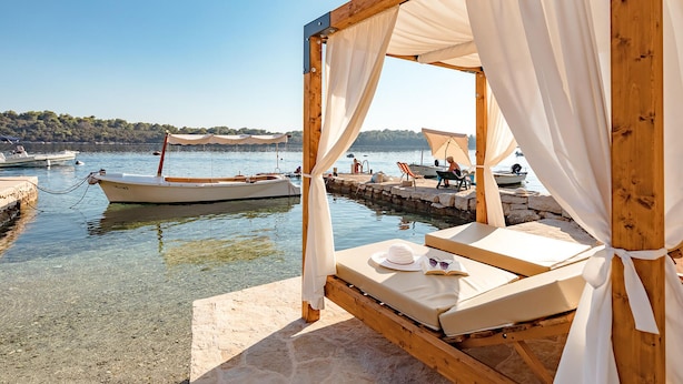 A wooden bed with white curtains, a hat, and sunglasses on it, overlooking a calm lake with boats and a dock. - Stunning home in Blato (Blato)
