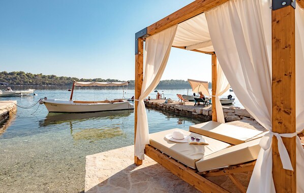 Relax in a serene waterfront setting with a cabana-style structure featuring a cushioned bench and table.