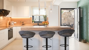 A modern kitchen with white cabinets, a wooden countertop, and three grey bar stools. - Stunning home in Blato (Blato)