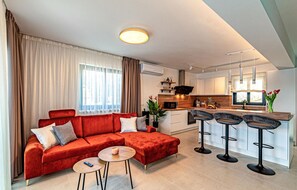 Relax in a cozy living area with a sofa and coffee table, complemented by a sleek kitchen with a central island and bar stools.