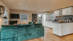 A modern living room with a green sofa, a fireplace, and a kitchen with white cabinets and a black countertop.