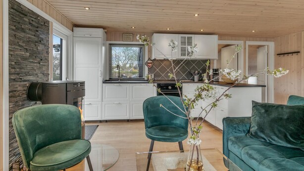 A modern kitchen with white cabinets and a black countertop, a dining area with green velvet chairs, and a view of the outdoors through a window.