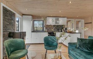 A modern kitchen with white cabinets and a black countertop, a dining area with green velvet chairs, and a view of the outdoors through a window. - Awesome home in Rønde with WiFi (Rønde)
