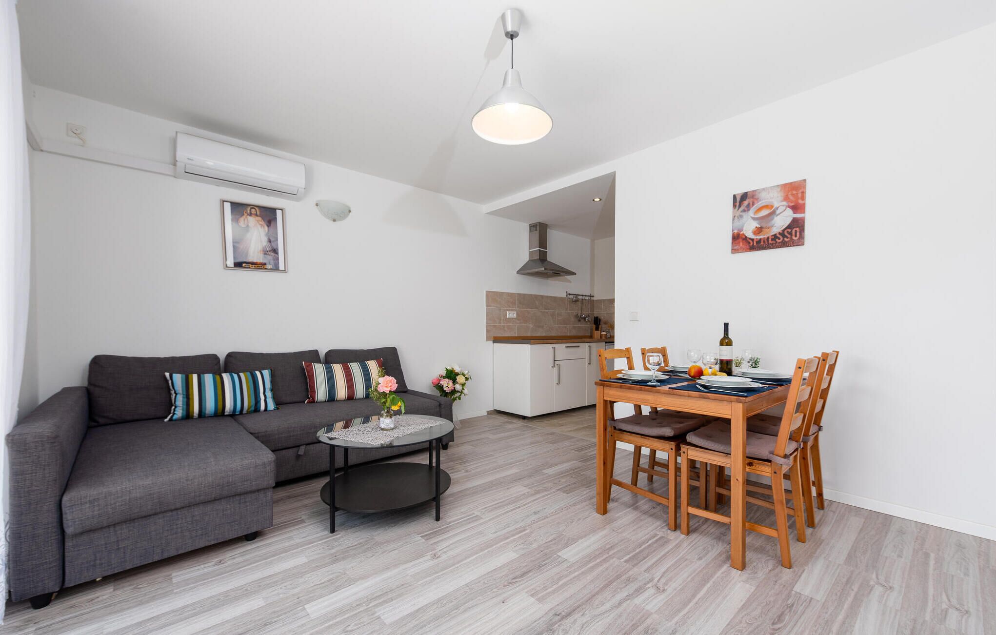 Ein Wohnzimmer mit grauem Sofa, einem Couchtisch und einem Essbereich mit Holzsesseln und einem Tisch für zwei Personen.