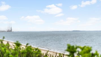 Une vue sur la côte, avec une plage de sable, une mer calme et des infrastructures industrielles situées au loin.