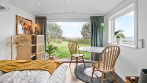 A bedroom with a bed, a wooden chair, a table, a hanging plant, and a view of the outdoors. - Lovely home in Esbjerg V with house sea view (Esbjerg V)
