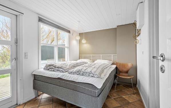 Un dormitorio con cama, una silla, un ventanal y una puerta.