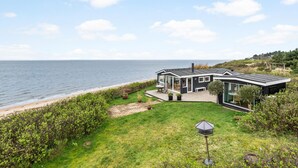 A modern coastal house with a deck overlooking the sea, a patio with outdoor furniture, and a garden area. - Lovely home in Esbjerg V with house sea view (Esbjerg V)