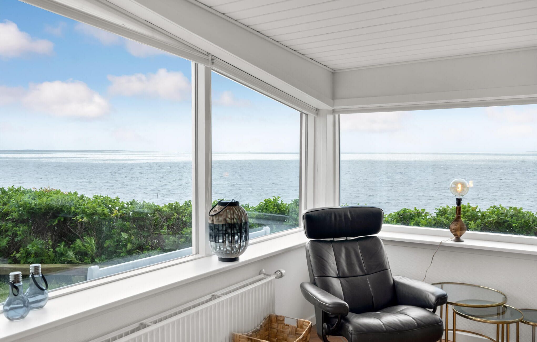 Ein Zimmer mit Meerblick, ein schwarzer Ledersessel, ein kleiner Tisch und eine Lampe.
