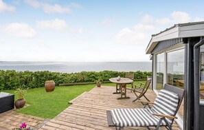 Eine Holzterrasse mit Tisch und Stühlen, eine Rasenfläche und Blick aufs Meer.