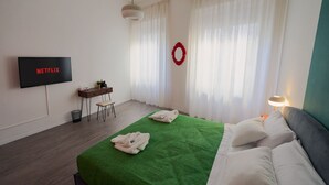A hotel room with a green bedspread, white pillows, a TV displaying 'NETFLIX', a desk with a chair, and a red wreath on the wall. - 2 minutes from rail station, bright flat in the centre on the town! CorsoItalia  (Arezzo)