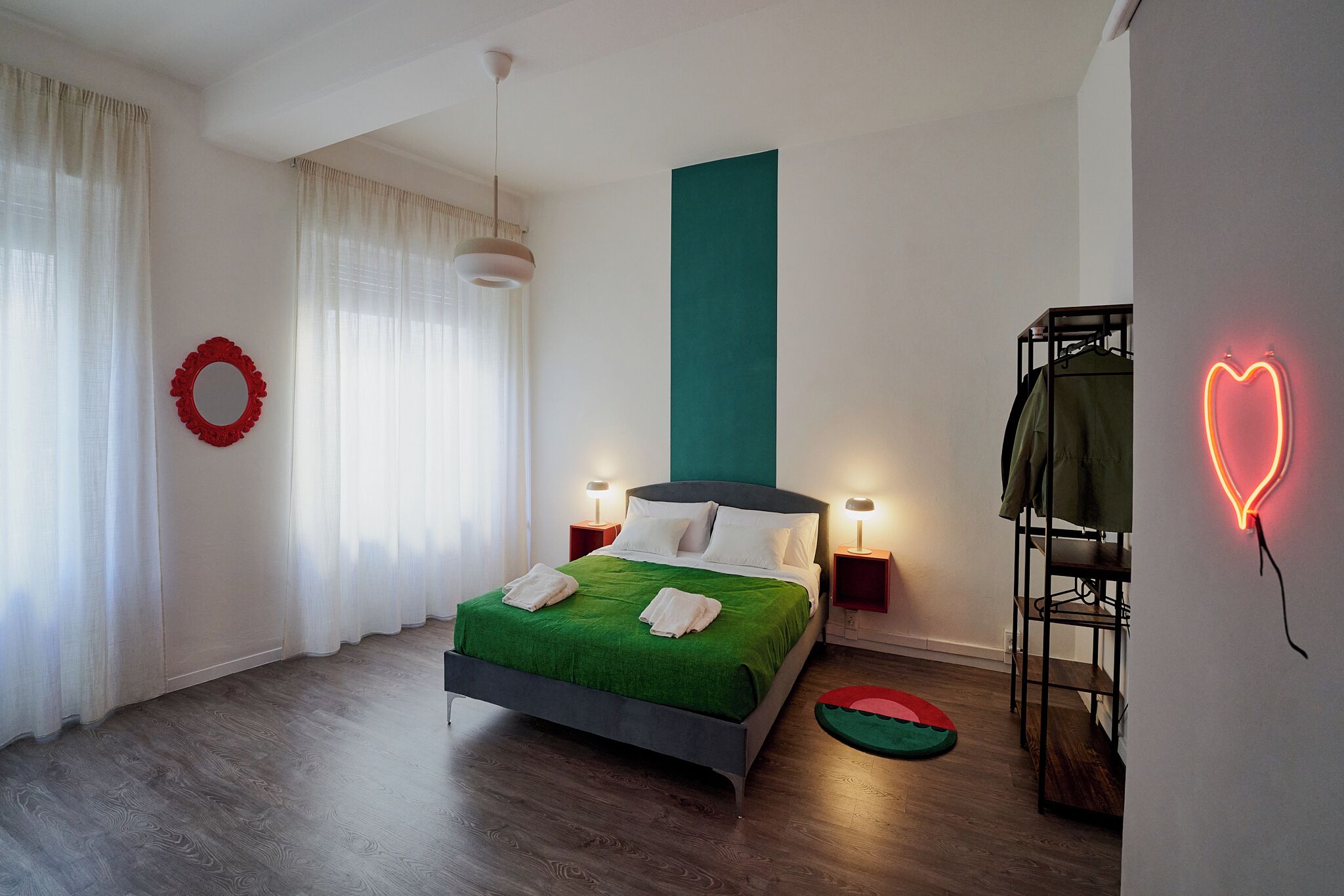 A modern bedroom with a bed, bedside lamps, a wall-mounted shelf, and a neon heart decoration.