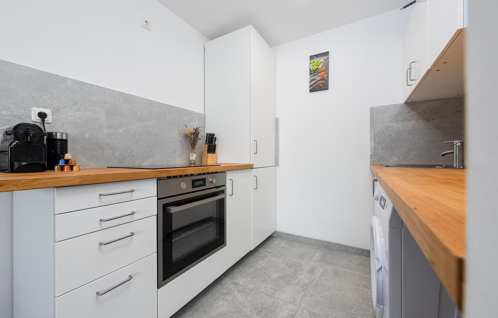 Une cuisine moderne avec des meubles blancs, un plan de travail en bois, un four encastré et un lave-vaisselle.