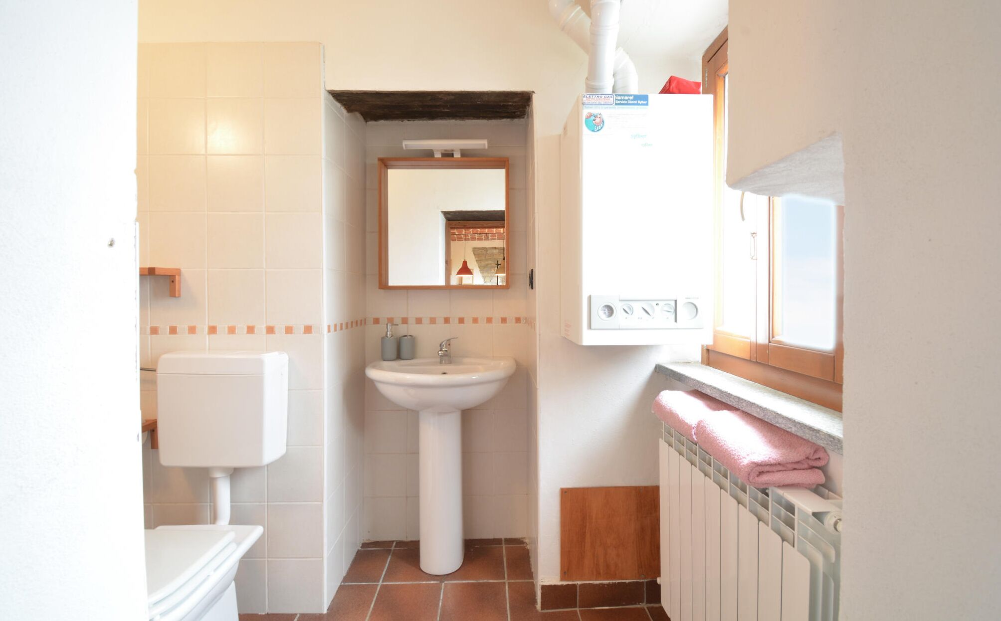Un baño pequeño con inodoro blanco, lavabo sobre pedestal, espejo y radiador.