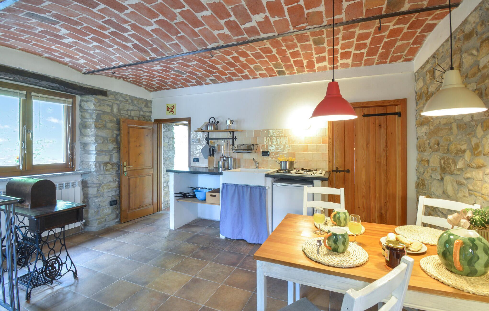 A kitchen with a brick ceiling, a dining table set with plates and glasses, and a window with a view of greenery.