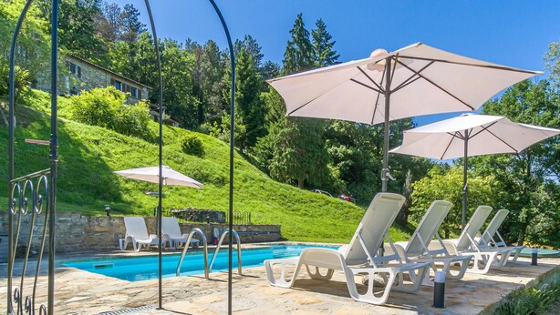 A poolside area with lounge chairs and umbrellas, a stone pool, and a hillside backdrop. - Awesome apartment in Monastero Bormida with house a panoramic view (Monastero Bormida)