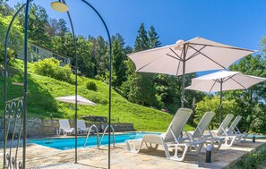 Ein Poolbereich mit Liegestühlen und Sonnenschirmen, einem Steingrund-Pool und einer Hügelkulisse.