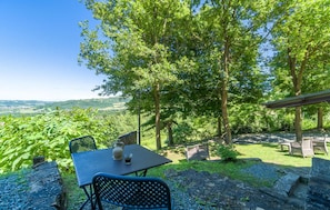 Relax in a serene outdoor setting with a table and chairs surrounded by lush greenery and a breathtaking view of rolling hills.