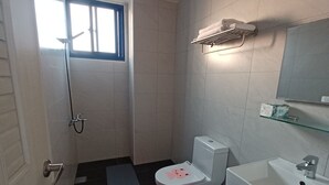Et lille badeværelse med toilet, håndvask og bruser. Der er et vindue, der giver naturligt lys, og en bøjle over håndvasken.