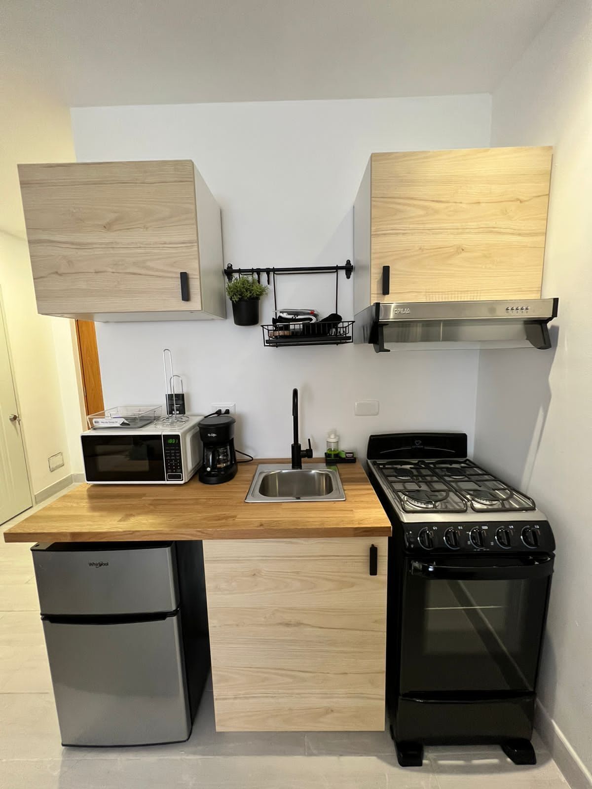 Una cucina compatta con microonde, macchina del caffè, lavello e fornello.
