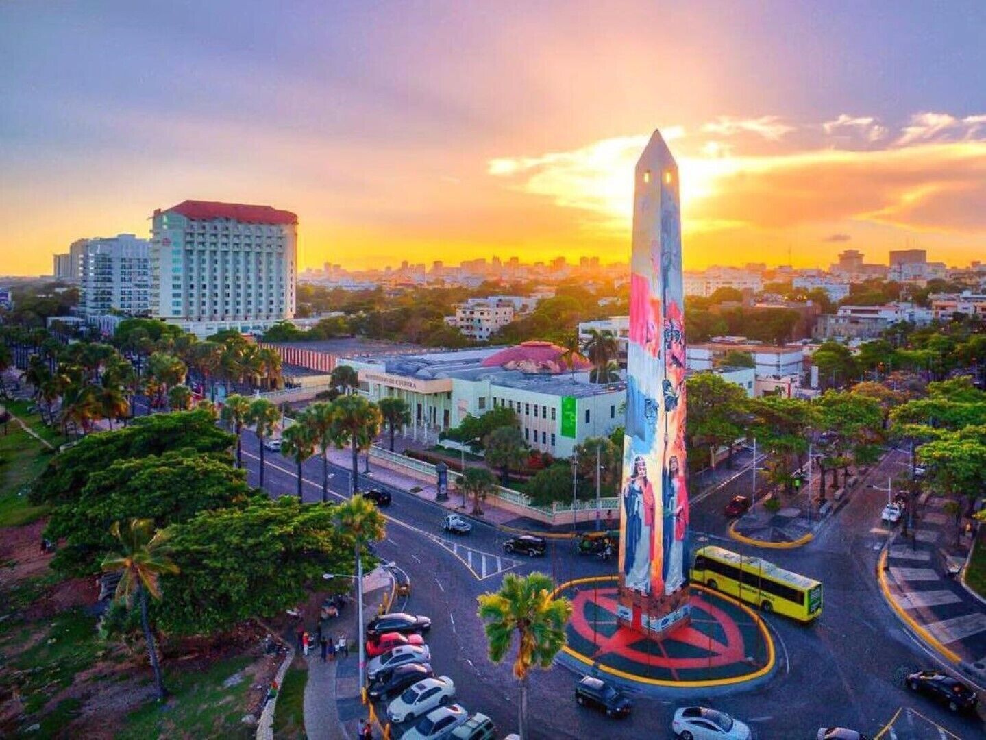 Een hoog monument met een ronde voet, omringd door een weg met auto's en een bus.