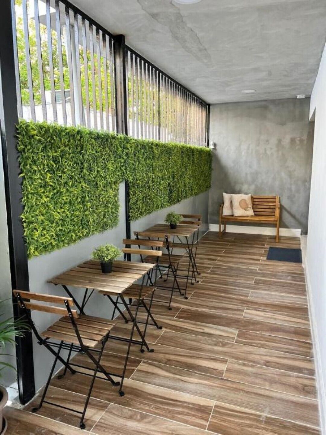 Ein moderner Außenbereich mit Holztischen und -bänken, einer vertikalen, grünen Gartenwand und einer Beton Decke.