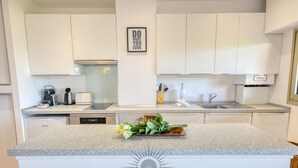 A modern kitchen with white cabinets, a granite countertop, a coffee maker, a toaster, and a sink. There's a framed motivational quote on the wall and a logo for Sunset Riviera Holidays on the countertop. - LA BADINE Studio AirCo Pool for 2 By Sunset (Antibes)