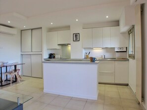 Een moderne keuken met witte kasten, een centraal eiland en een eethoek met een tafel en stoelen.