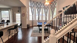A spacious living area with a wooden floor, a pool table, and a staircase with black railings. - Beautiful Home W/Heated Pool- Sleeps 16, Pets & Small Events Allowed W/Approval  (Mansfield)