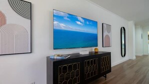 A modern living room with a large flat-screen TV mounted on the wall, a black console table with decorative items, and framed artwork on the walls.
