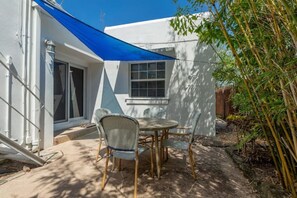 Relax on the patio with a table and chairs under a shaded area, adjacent to a building with a window and door.