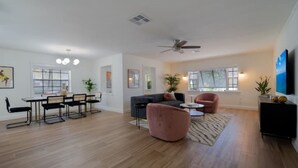 A spacious living area with a dining table, chairs, a sofa, a pink armchair, and a ceiling fan.