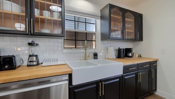 A modern kitchen with black cabinets, a white sink, and a wooden countertop.