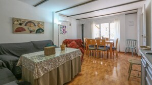 Een woonkamer met een bank, een salontafel met glazen blad, een eethoek met houten stoelen en een tafel, en een keuken met een fornuis.