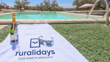 Une scène de bord de piscine avec une bouteille de champagne, un verre et des lunettes de soleil posés sur une serviette, et l’inscription « Ruralidays, votre chez-vous en Andalousie ».