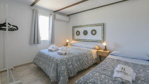 Een slaapkamer met twee bedden, een raam met gordijnen, een luchtverkoeler aan de muur en een ingelijst schilderij boven de bedden.