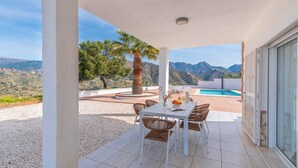A covered outdoor dining area with a table and chairs, a pool, and a view of mountains. - Villa Tres Flores Cómpeta by Ruralidays (Málaga)