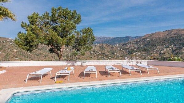 A poolside area with lounge chairs and a view of a mountainous landscape. - Villa Tres Flores Cómpeta by Ruralidays (Málaga)