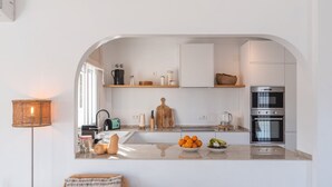 A modern kitchen with white cabinets, a built-in oven, and a countertop with fruits and vegetables. - Villa Tres Flores Cómpeta by Ruralidays (Málaga)
