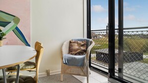 Ein Balkon mit einem Korbstuhl, einem kleinen Tisch mit Kissen und Blick auf eine Wohngegend.