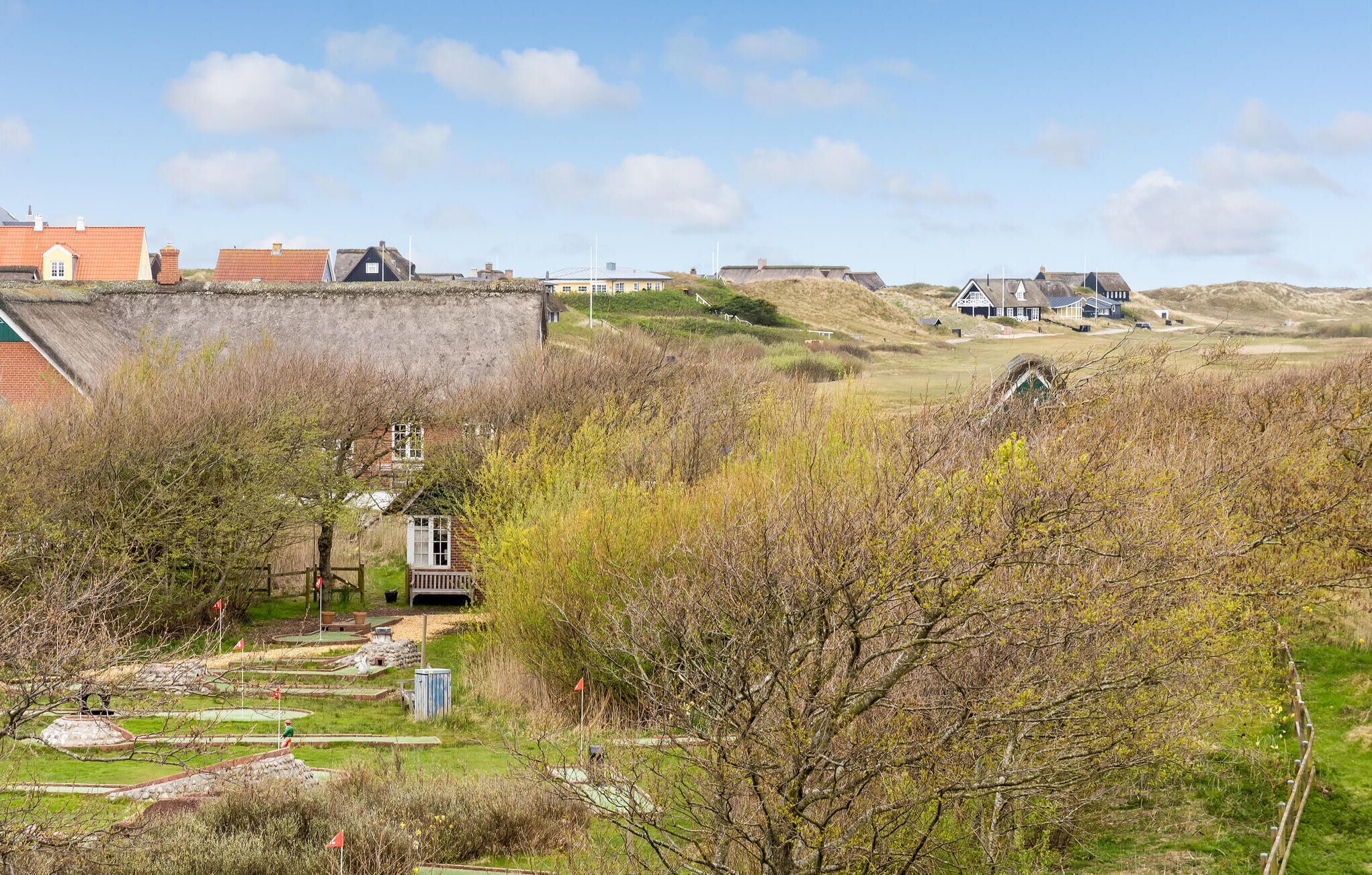 Uma vila costeira com casas tradicionais, um campo de golfe e uma pequena ponte de madeira.