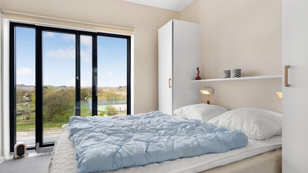 Ein Schlafzimmer mit einem großen Bett, einem Kleiderschrank, einem Nachttisch mit Lampe und Blick ins Freie.