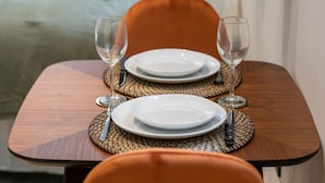 A dining table set with two plates, two wine glasses, and cutlery on woven placemats. - The O1 - room 1 - Opera - 26m² (Lyon)