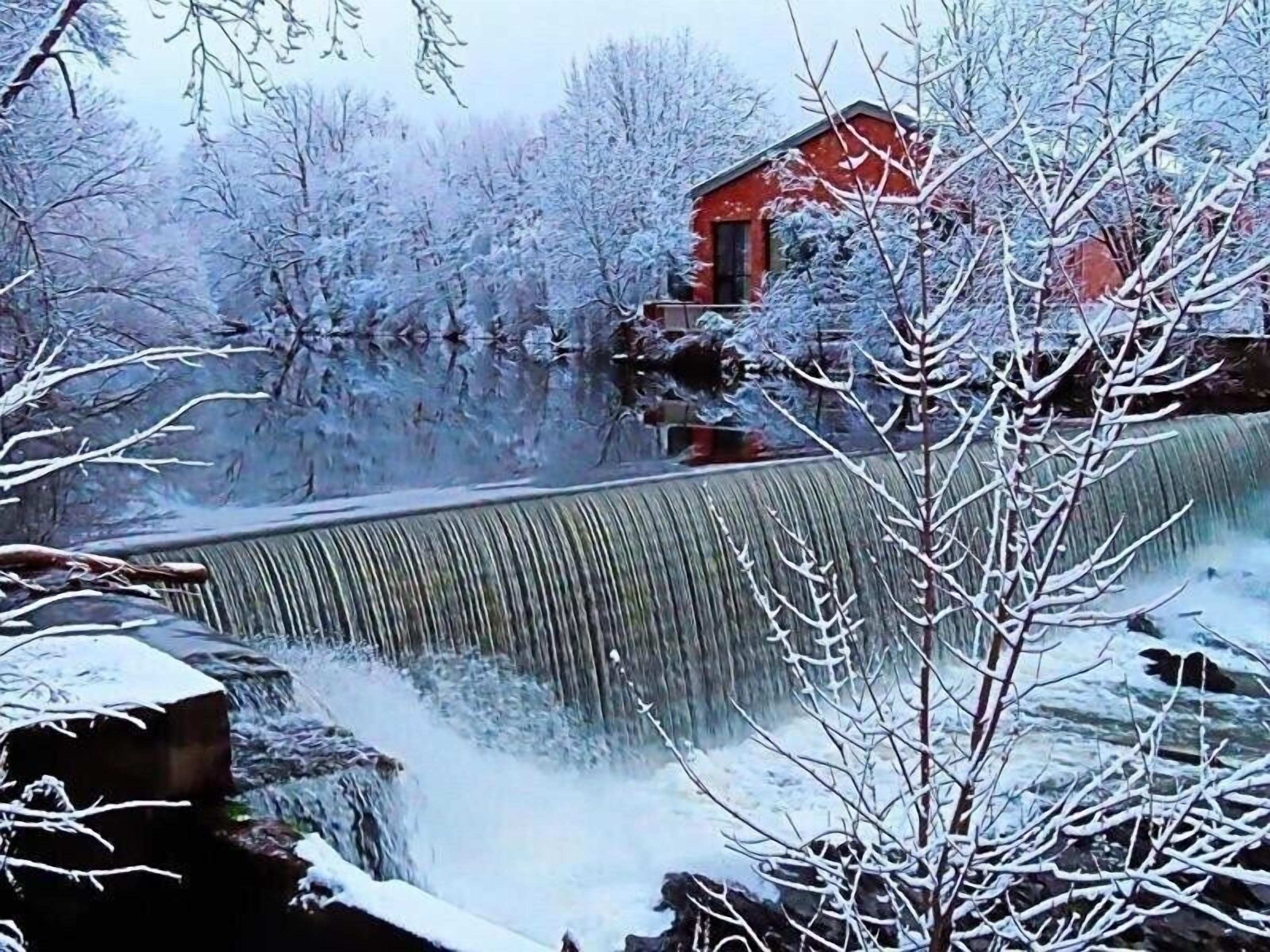 A snow-covered landscape with a waterfall and a red building.