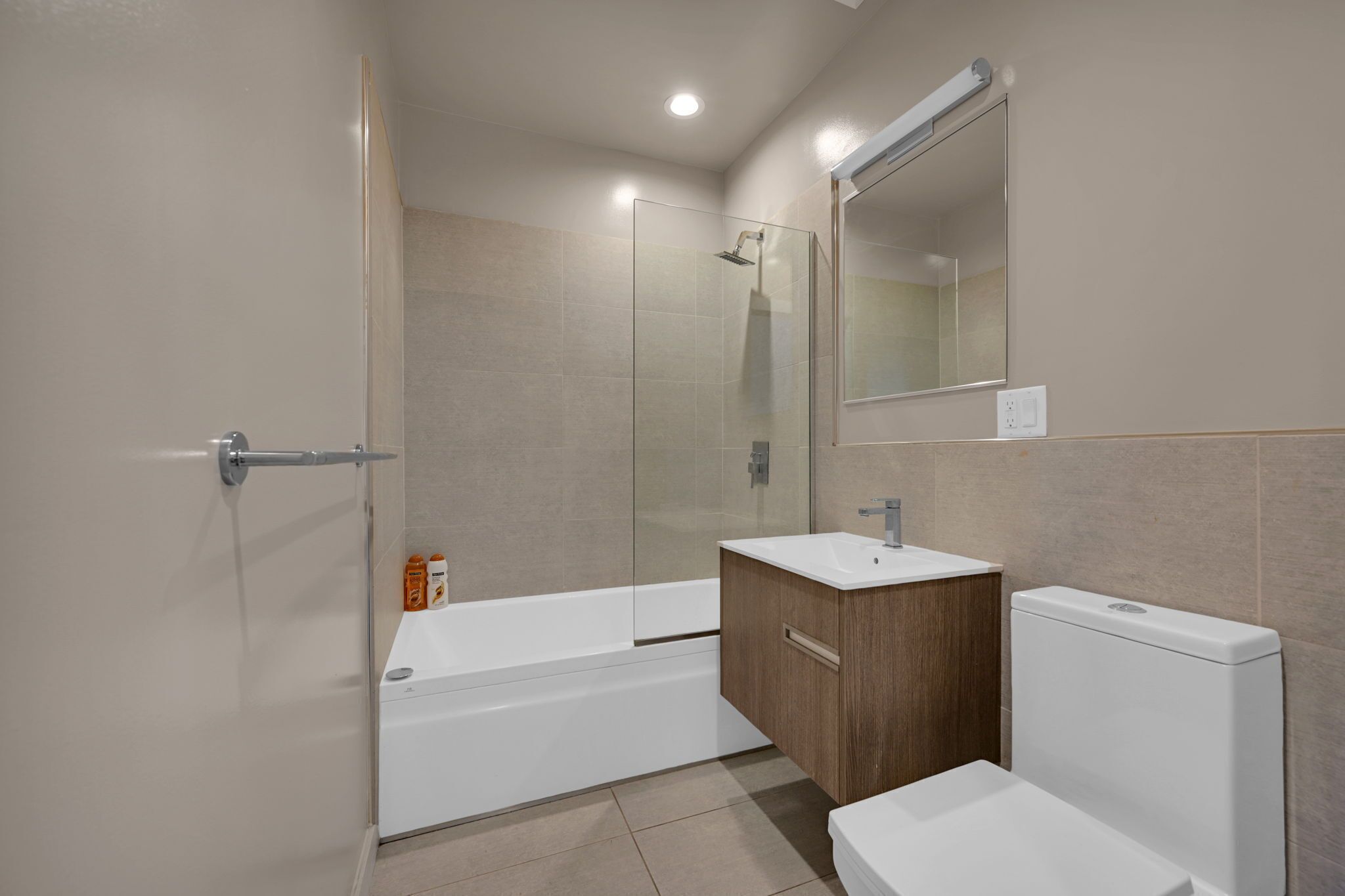 Un baño moderno con ducha envuelta en vidrio, tocador de madera y inodoro blanco.