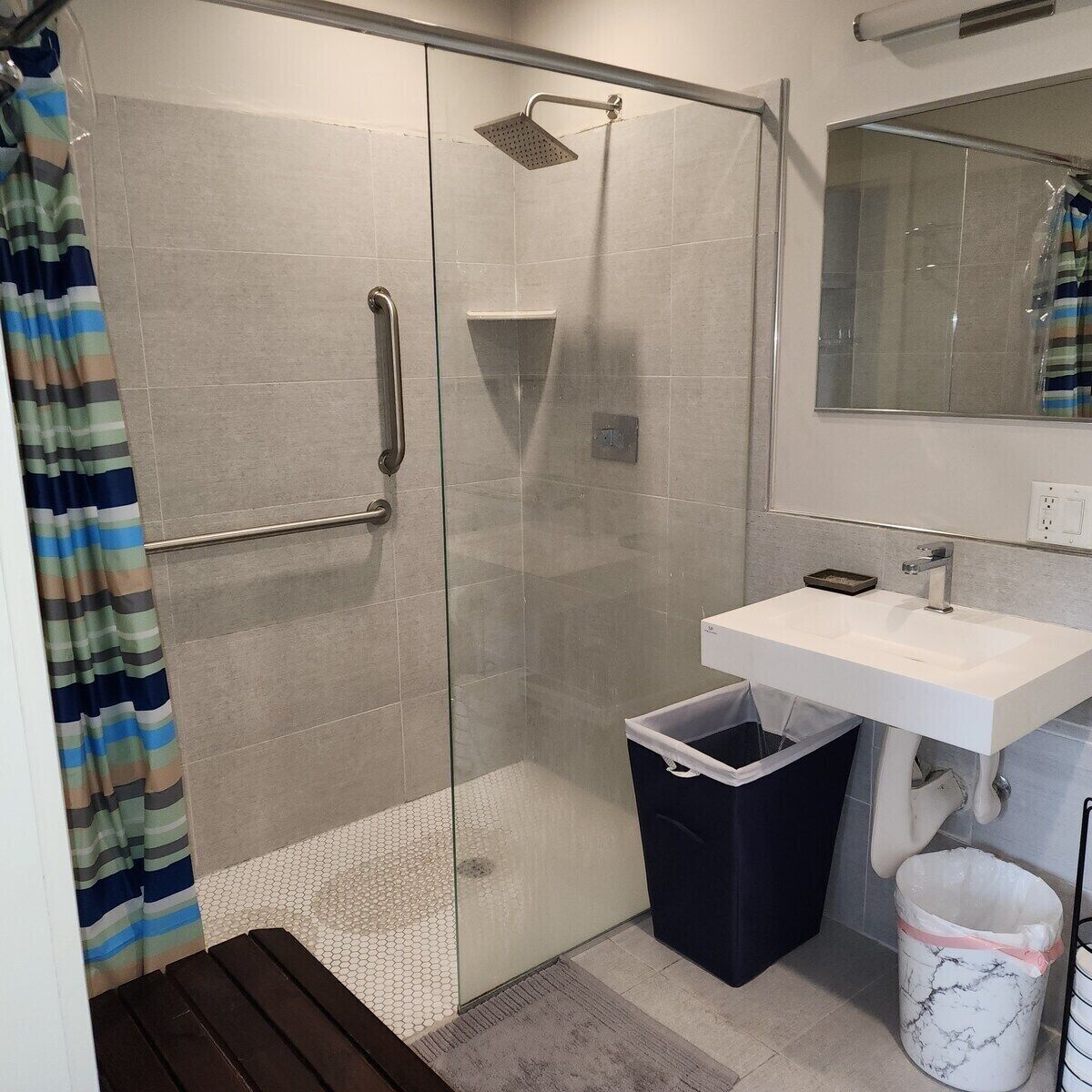 Un baño moderno con cabina de ducha de vidrio, un lavabo blanco y un cubo de basura de mármol.