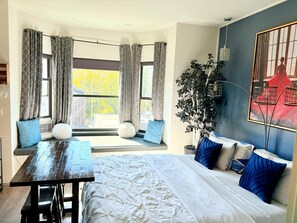 A modern bedroom with a large bed, a dining table, and a view of trees through the windows. - Beacon Hotel (Beacon)