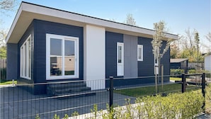Een modern huis met twee verdiepingen, een donkere buitenkant, witte decoratielijsten en een zwart metalen hek.