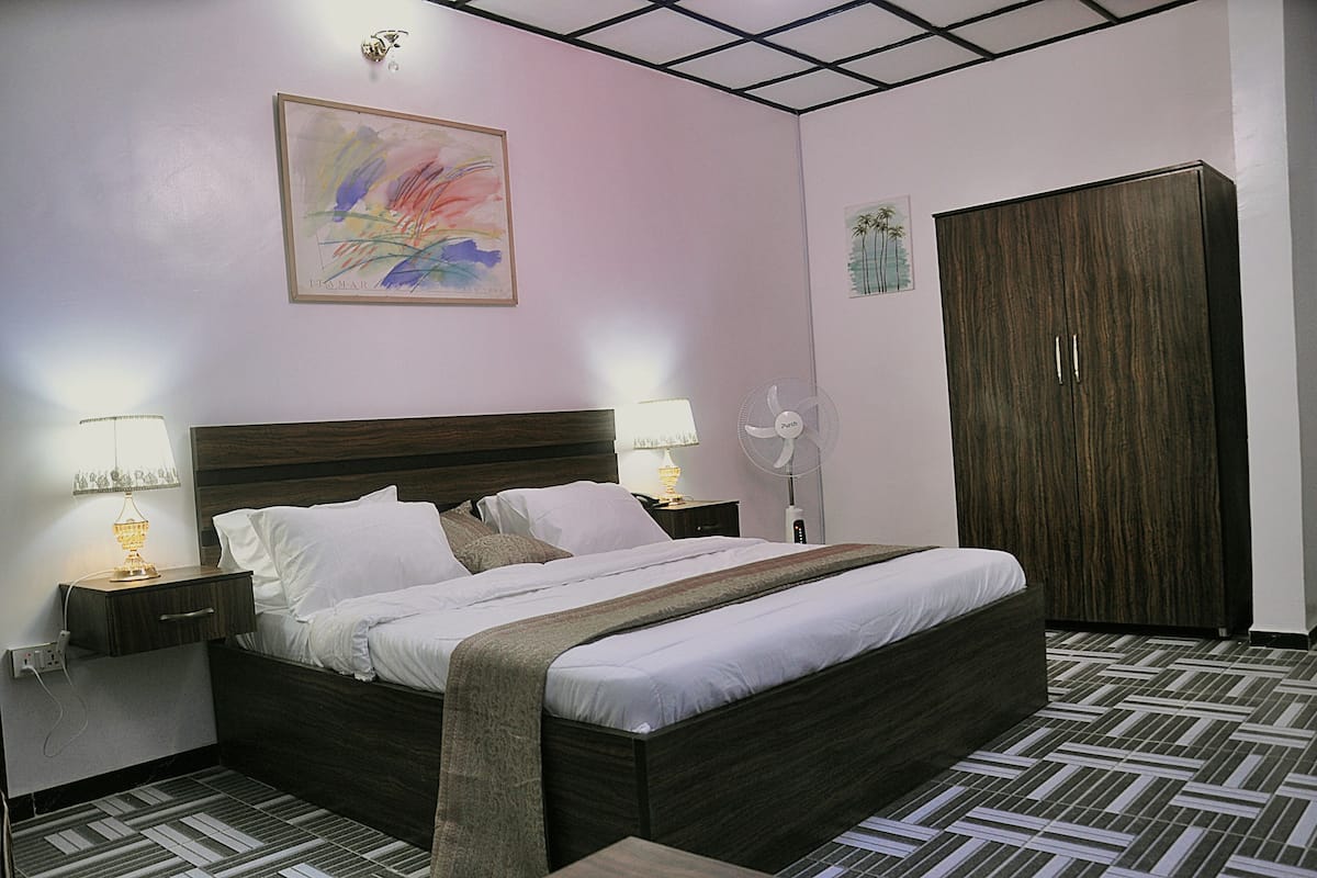 A neatly arranged hotel room with a large bed, bedside lamps, a wardrobe, and a wall-mounted artwork.